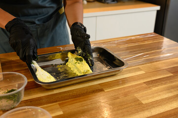 Close up of hands blending chopped herbs into softened butter on a metal tray