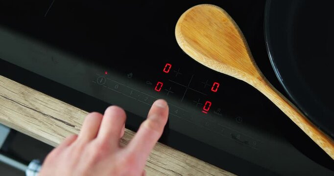Cook presses finger on modern hob screen and turns on cooking mechanism setting mode. Man prepares to create dish and keeps frying pan on equipment surface