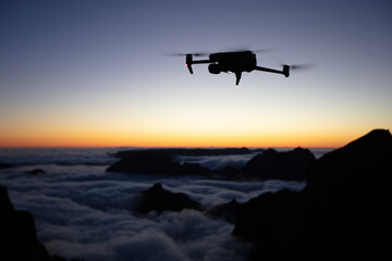 Drone Silhouette in Sunset Light. High Mountains Peaks on Background with Clouds in a Valley. Clear...