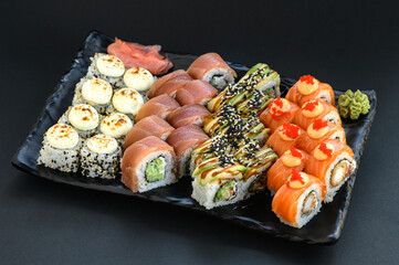 Assorted sushi rolls beautifully arranged on one plate over a black background. Elegant Japanese cuisine set, ideal for restaurant menu or premium food presentation.
