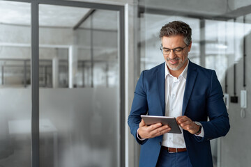 Executive man in suit working using computer for financial business banking work. Smiling senior mature Indian or Latin entrepreneur businessman looking at digital tablet screen in office. Copy space 
