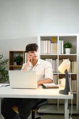 Confident young entrepreneur talking on phone working at laptop in a modern home office