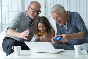 Two old men with granddaughter playing on laptop 