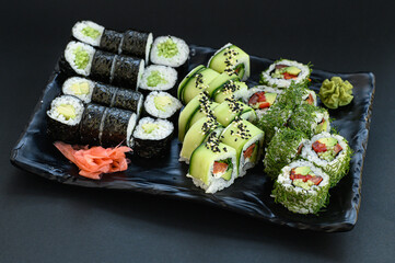 Assorted vegan sushi rolls beautifully arranged on one plate over a black background. Elegant Japanese cuisine set, ideal for restaurant menu or premium food presentation.