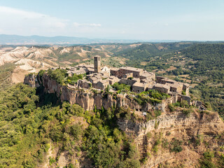 Aerial shot of a small Italian town near Civita di Bagnoregio, with terracotta-roofed houses, a fortified gate, and a lush rural landscape. The scene captures Italy’s cultural and historical essence.