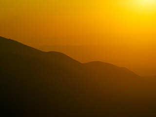 Aerial view Pirin Mountains, Bulgaria, during summer golden hour, captured from above, layered silhouettes of ridges fading into distance under glowing sky. Travel nature concept
