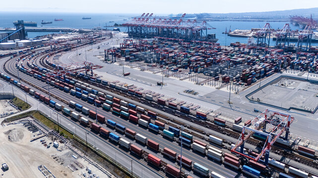 High-angle view of towering shipping cranes moving containers from a large cargo ship docked at a seaport. The deep blue ocean and colorful containers create a dynamic logistics scene.