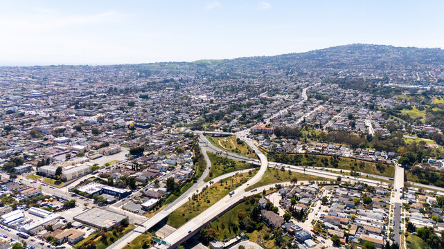 Wide drone shot capturing a sprawling residential neighbourhood in Long Beach, California, with visible highway lanes, intersections, and surrounding hills in the background.