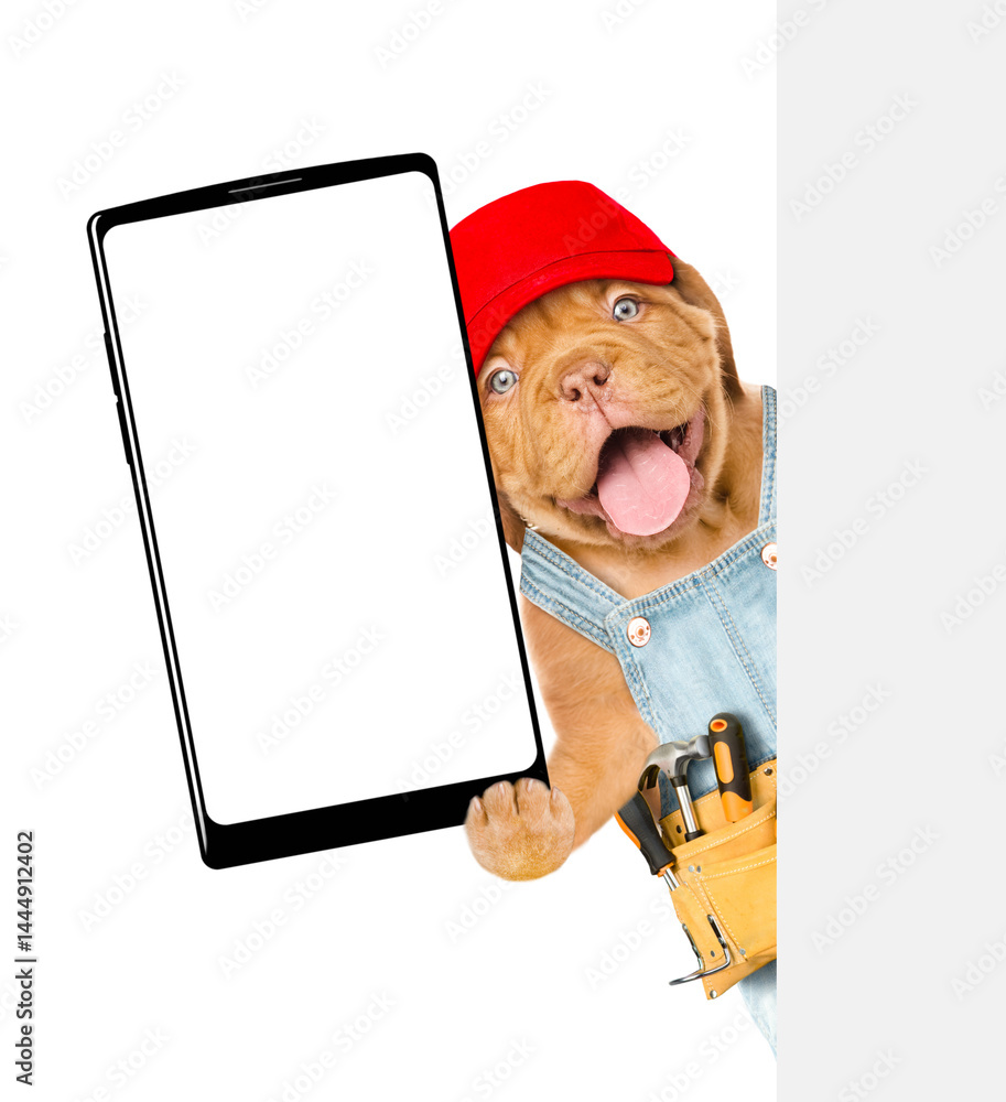 Aufkleber Happy Mastiff puppy wearing red cap and denim overalls with tool belt shows big smartphone with blank screen behind blank wihte banner. Empty space for text. Isolated on white background