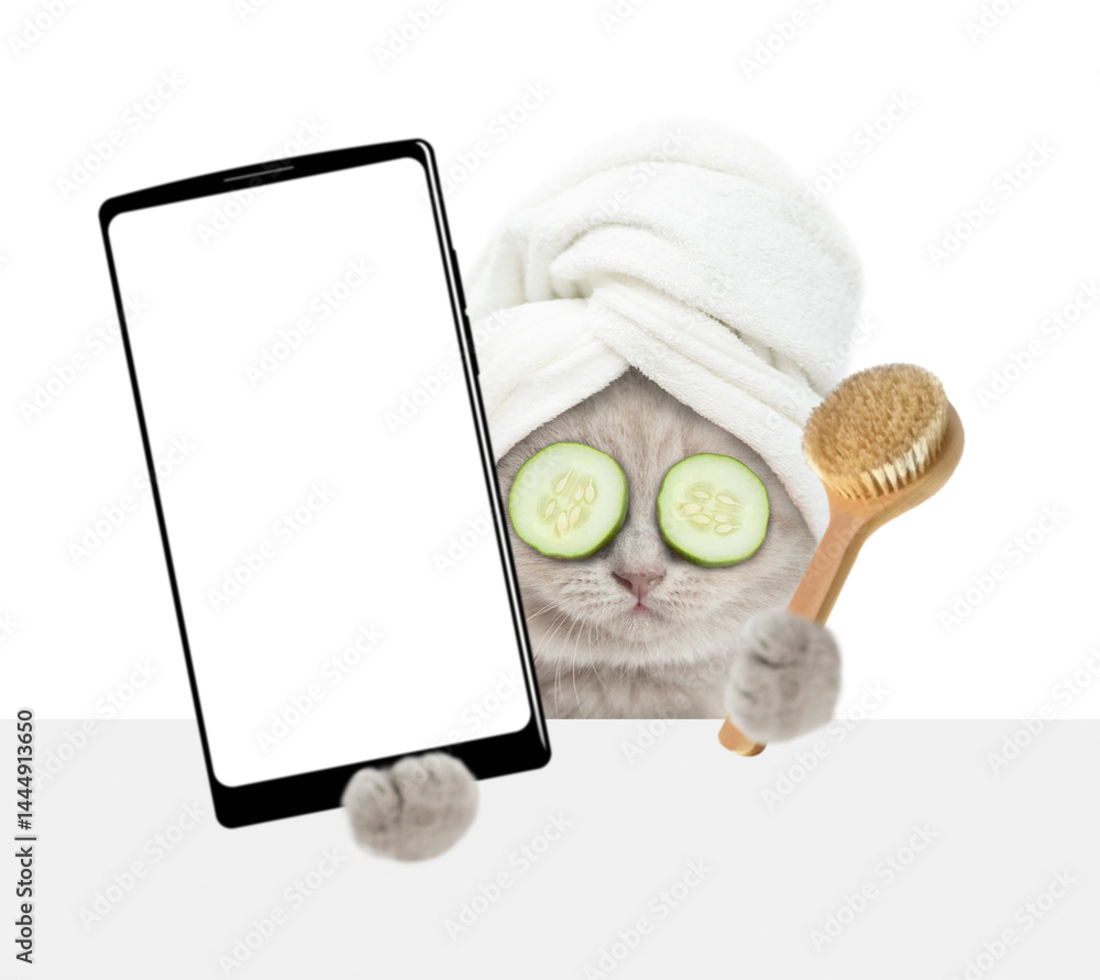 Aufkleber Cute tiny kitten with towel on it head holds  shower brush and big smartphone with white blank screen in it paw above blank white banner. isolated on white background