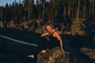 A woman practicing yoga at sunset in nature, barefoot and dressed in leg warmers and a hat,surrounded by rocks and forest. The scene reflects meditation, health, inner balance, and harmony with nature