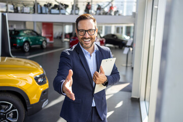 Successful deal in a car showroom, young confident sales man reaching out for a handshake.