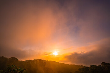 stunning mountainous landscape at sunrise with vibrant orange and pink hues illuminating the clouds against a blue sky. layer of mist settled in the valley, giving the scene a dreamy.