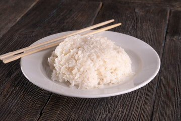 Plate with white rice on black background. Chopsticks