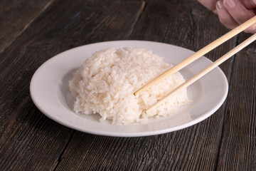 Plate with white rice on black background. Chopsticks