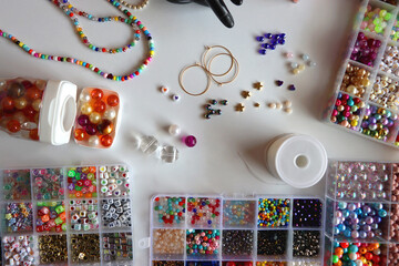 Hand figurine, colorful friendship bracelets, necklaces, various beads and DIY supplies on the table. Making jewelry at home. Flat lay.