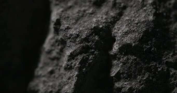 Dark close-up of volcanic rock with rough porous surface and shadow play