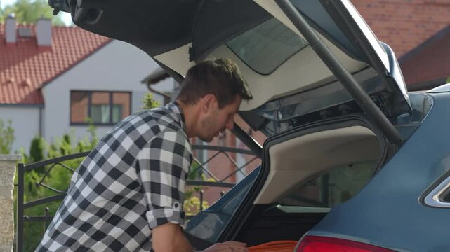 Man loading orange suitcase into car trunk before journey. Packing luggage for travel