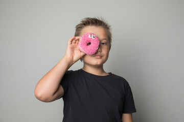 Young child boy holding testy donut. Kid in black t-shirt with sweet food indoor