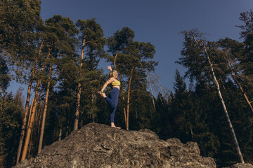 A woman meditating and practicing yoga on top of a rock at sunset, embracing wellness, mindfulness,...