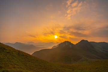 Aerial view of serene sunset casts a golden glow over rolling hills and distant mountain peaks,...