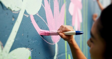 Woman, hand or painting on wall art for mural, creativity or community service at building. Artist, paintbrush or outdoor with color for floral decor, creative process or flowers for aesthetic design © peopleimages.com