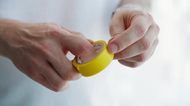 A roll of electrical tape close-up in hands.
An electrician unwinds a roll of electrical tape.
Electrical work.
Electrical work master
