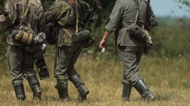 German soldiers walk on grass field, infantry wear authentic WWII Wehrmacht and SS uniforms, including field grey camouflage patterns. Third Reich army. Historical reenactment of World War 2 battle
