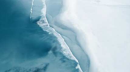 Abstract natural patterns formed by white surf foam and receding turquoise water on the shoreline of a sandy beach, seen from above.