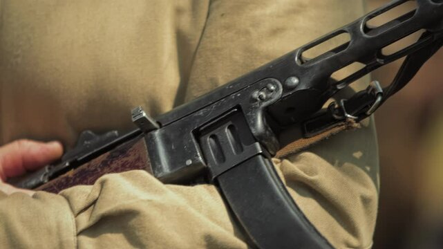 Close-up Red Army soldier holds Soviet PPSh-41 submachine gun during Great Patriotic War historical reenactment. Weapon of Second World War. WWII military show. Man in Khaki gymnasterka type shirt