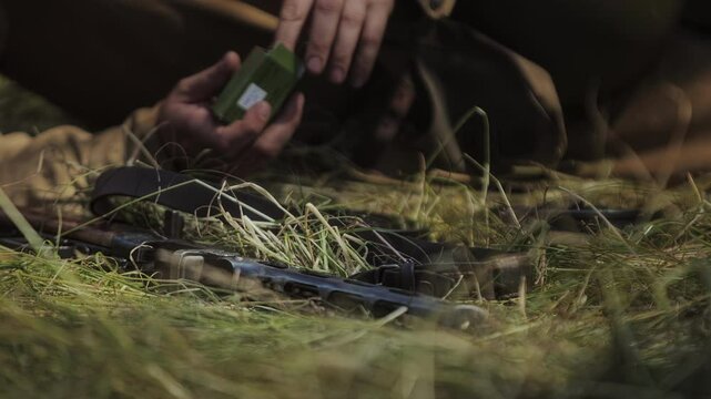 Camera angle looks through grass at Soviet PPSh 41 submachine gun. Great Patriotic War historical reenactment. Red Army Russian soldier lies and rests in shade during simulated WW2 event.