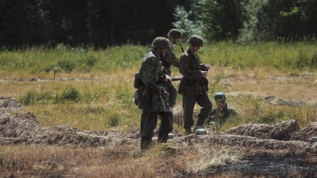 German Waffen-SS soldiers walk across field along trenches during World War Two reenactment before combat simulation. WWII historical reconstruction, event show. Defense, waiting for Allied offensive