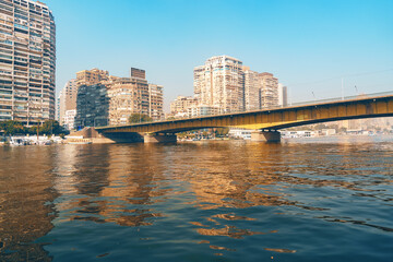 Obraz premium Cityscape view of a bridge spanning the Nile River with modern buildings along the waterfront in Cairo during a clear day
