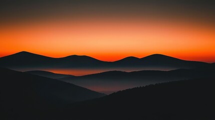 Obraz premium Silhouetted mountain ranges are under a vibrant orange sunset sky