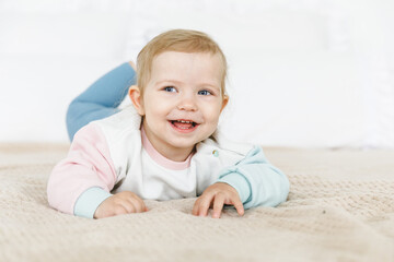 Fototapeta premium Smiling baby 6-12 months old lying on his stomach on a white bed.
