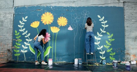 Women, creative or friends painting on wall for mural, drawing flowers or community service at...
