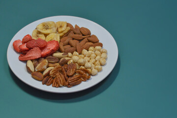 A variety of nuts and dried fruits on a plate on blue background. Hazelnuts, pecans, brazil nuts, almonds, dried strawberries and bananas. The concept of nutrition, diet, healthy eating and sports