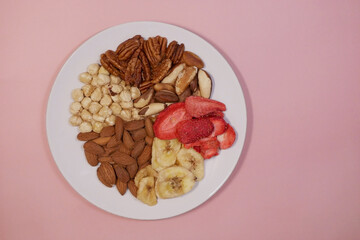 A variety of nuts and dried fruits on a plate on pink background. Hazelnuts, pecans, brazil nuts, almonds, dried strawberries and bananas. The concept of nutrition, diet, healthy eating and sports