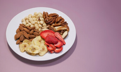 A variety of nuts and dried fruits on a plate on pink background. Hazelnuts, pecans, brazil nuts, almonds, dried strawberries and bananas. The concept of nutrition, diet, healthy eating and sports