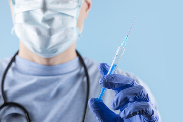 A doctor wearing a mask and gloves measures out the vaccine before administering an injection
