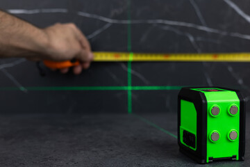 hands of a worker who measures the width of a tabletop with a tape measure and a laser