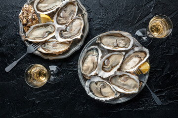 Fresh raw oysters on ice, overhead flat lay shot of two platters with lemon and champagne on a black slate background