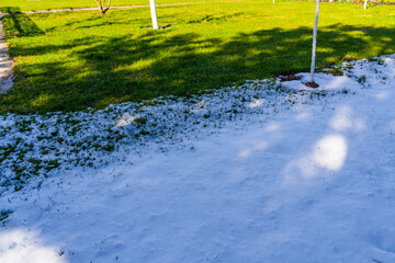 Snow melting in spring on a sunny morning. Half of the lawn is covered with snow and half with...