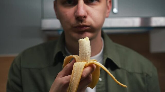 A man in a green rabbi chews a banana.
A hungry guy.
A healthy snack with a banana. A banana in the hands of a guy.
A young man with a ripe banana