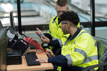 Machine learning. Electrical engineer. Works on desktop computer. Team of male engineers training Programmable logic controller in workshop. Industrial computer concept