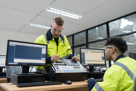 Machine learning. Electrical engineer. Works on desktop computer. Team of male engineers training Programmable logic controller in workshop. Industrial computer concept