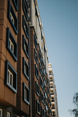 Contemporary apartment building featuring a unique architectural design and geometrically styled windows, captured beneath a vibrant blue sky. Ideal for depicting modern urban lifestyle.