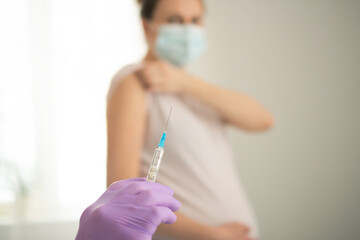 Expecting mother getting routine vaccine during pregnancy. Focus on healthcare worker's hands...