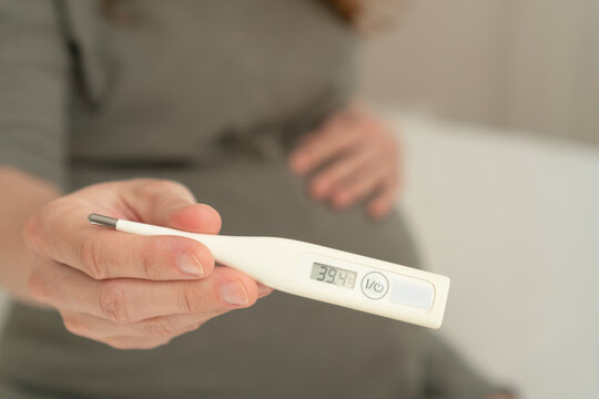 Pregnant female carefully checking temperature with thermometer. Important health precaution for expecting mothers feeling unwell.