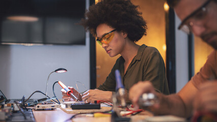 Young woman soldering a circuit boards in her tech office